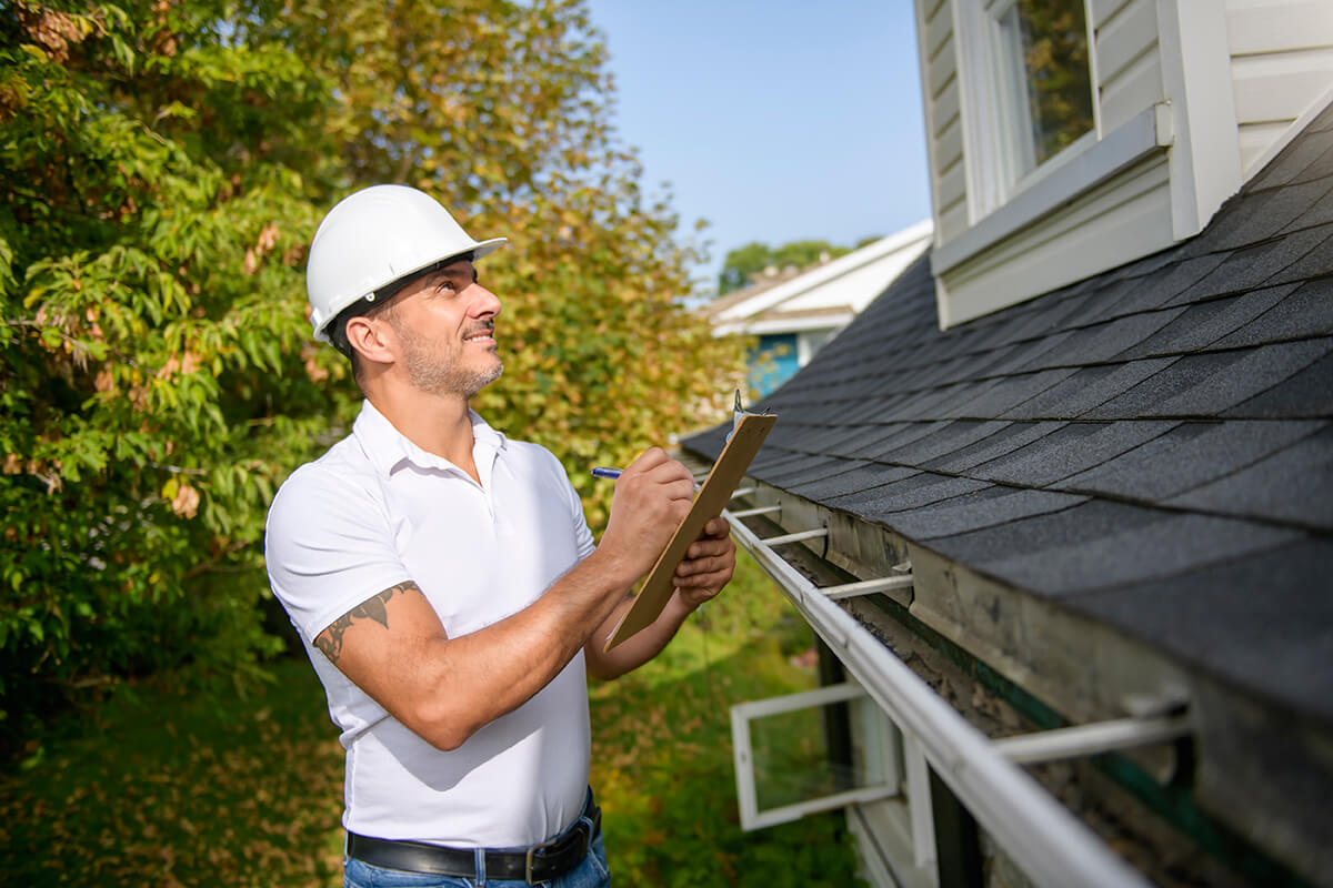 Worker on a ladder estimating roof quality for insurance policies