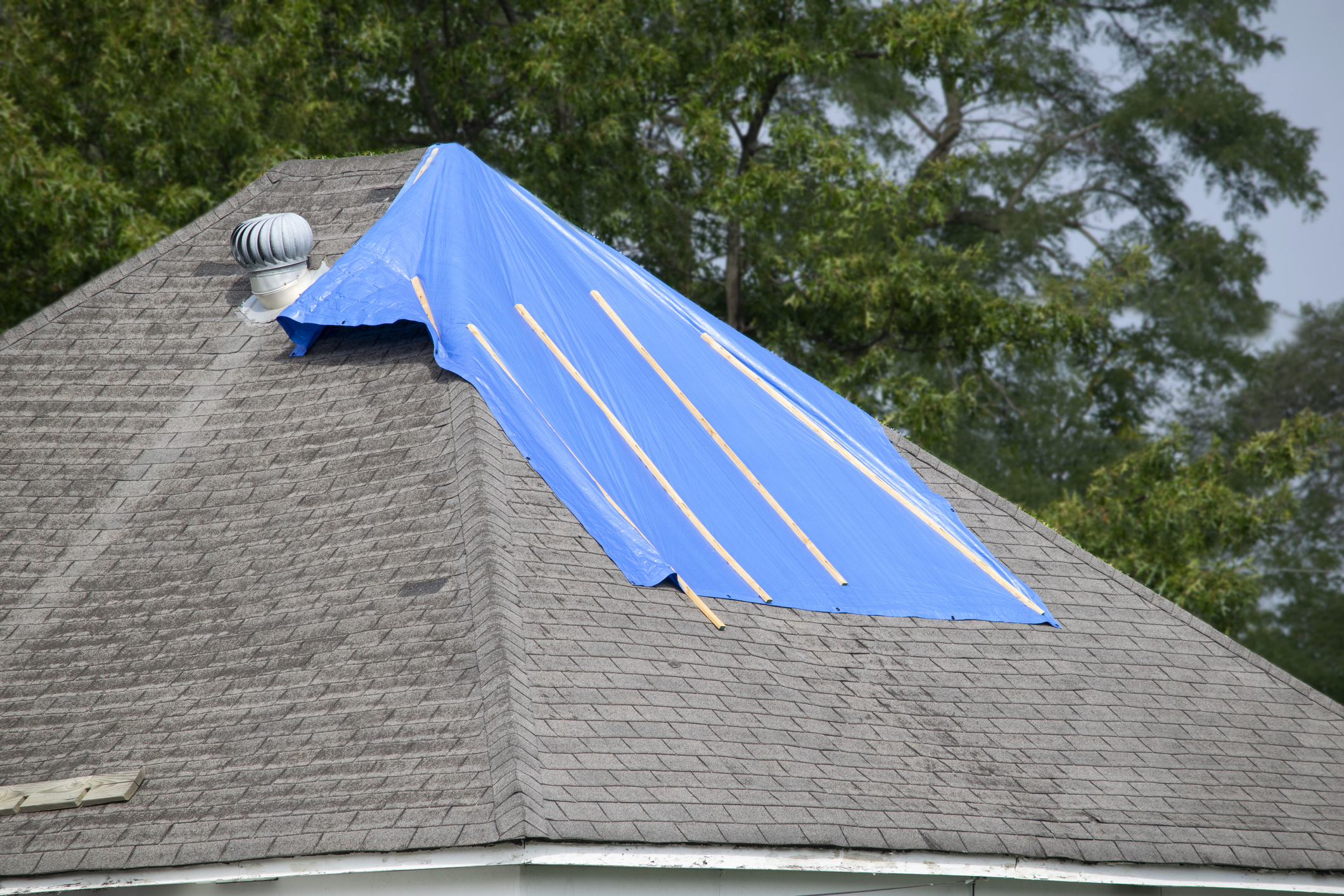 Damaged roof with bad shingles partially covered with a tarp